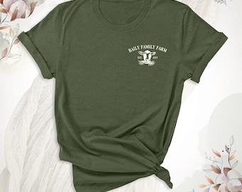 Könnte beinhalten: Ein olivgrünes Kurzarm-T-Shirt mit einer weißen Grafik auf der linken Brust. Die Grafik zeigt einen Kuhkopf mit dem Text "BAILY FAMILY FARM" in einem Bogen darüber und "EST. 2025" unter der Kuhillustration in einer klaren, weißen Schrift.