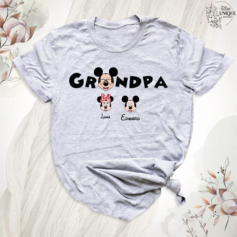Puede incluir: Camiseta gris con la palabra "Grandpa" en letras negras. Mickey Mouse aparece en la palabra "Grandpa" con Minnie Mouse y otro Mickey Mouse debajo de la palabra. Los nombres "Luna" y "Edward" est&aacute;n escritos debajo de los personajes.