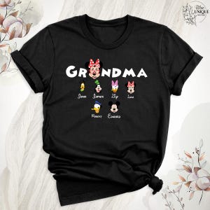 Puede incluir: Camiseta negra con la palabra "Grandma" en letras blancas y un lazo rojo. Hay seis personajes de dibujos animados debajo de la palabra, cada uno con un nombre debajo: John, James, Lily, Luna, Robert y Edward.