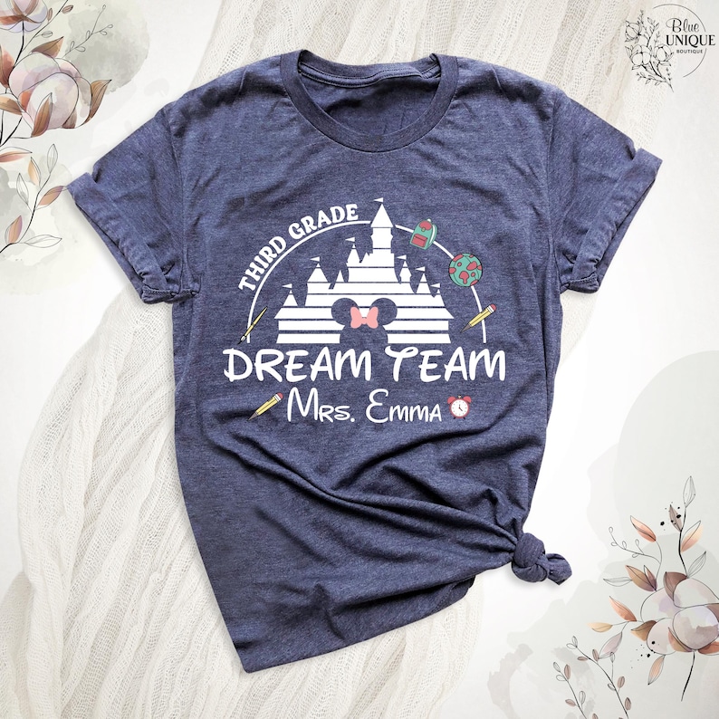 May include: Navy blue t-shirt with a graphic design for a third-grade teacher. The design includes a castle, a Minnie Mouse bow, and the words "Third Grade Dream Team Mrs. Emma". A pencil and a clock are also included in the design.