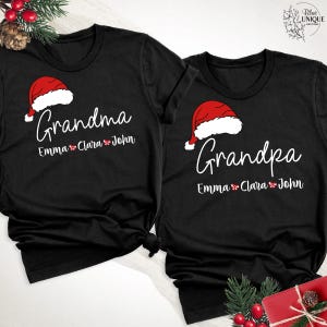 以下が含まれることがあります： クリスマスをテーマにしたデザインの黒いTシャツ2枚。「おばあちゃん」とサンタ帽子のグラフィックがプリントされたものと、「おじいちゃん」とサンタ帽子のグラフィックがプリントされたもの。どちらのシャツにもEmma、Clara、Johnの名前が記載されています。