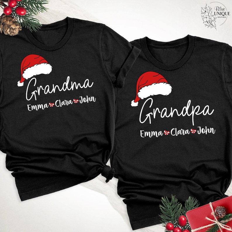 以下が含まれることがあります： クリスマスをテーマにしたデザインの黒いTシャツ2枚。「おばあちゃん」とサンタ帽子のグラフィックがプリントされたものと、「おじいちゃん」とサンタ帽子のグラフィックがプリントされたもの。どちらのシャツにもEmma、Clara、Johnの名前が記載されています。