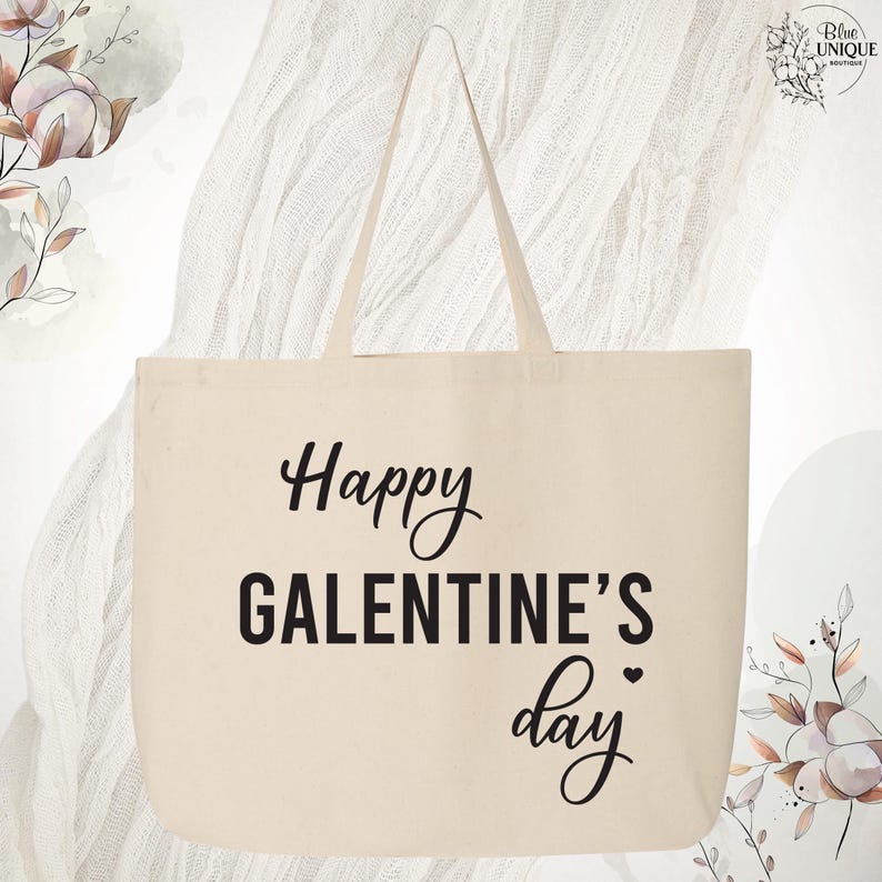 May include: Cream-colored tote bag with the text "Happy GALENTINE'S day" in black script and block letters. The bag has two handles and is made of a sturdy fabric. The design is simple and elegant.