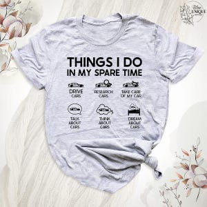 Op de afbeelding: Grijs T-shirt met de tekst "THINGS I DO IN MY SPARE TIME" en een lijst met autogerelateerde activiteiten, waaronder "DRIVE CARS", "RESEARCH CARS", "TAKE CARE OF MY CAR", "TALK ABOUT CARS", "THINK ABOUT CARS" en "DREAM ABOUT CARS".