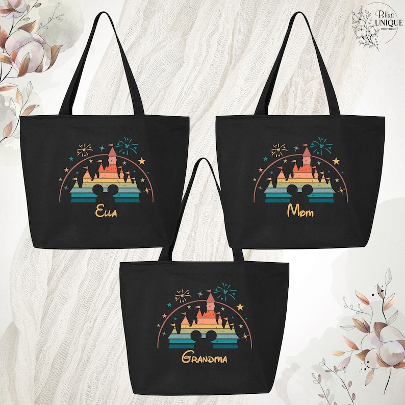 May include: Three black canvas tote bags with a retro rainbow design of a castle with fireworks and a Mickey Mouse ear silhouette. The bags are personalized with the names "Ella", "Mom", and "Grandma".