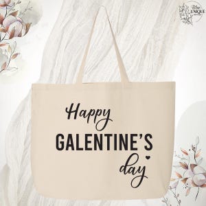 May include: Cream-colored tote bag with the text "Happy GALENTINE'S day" in black script and block letters. The bag has two handles and is made of a sturdy fabric. The design includes a small heart.