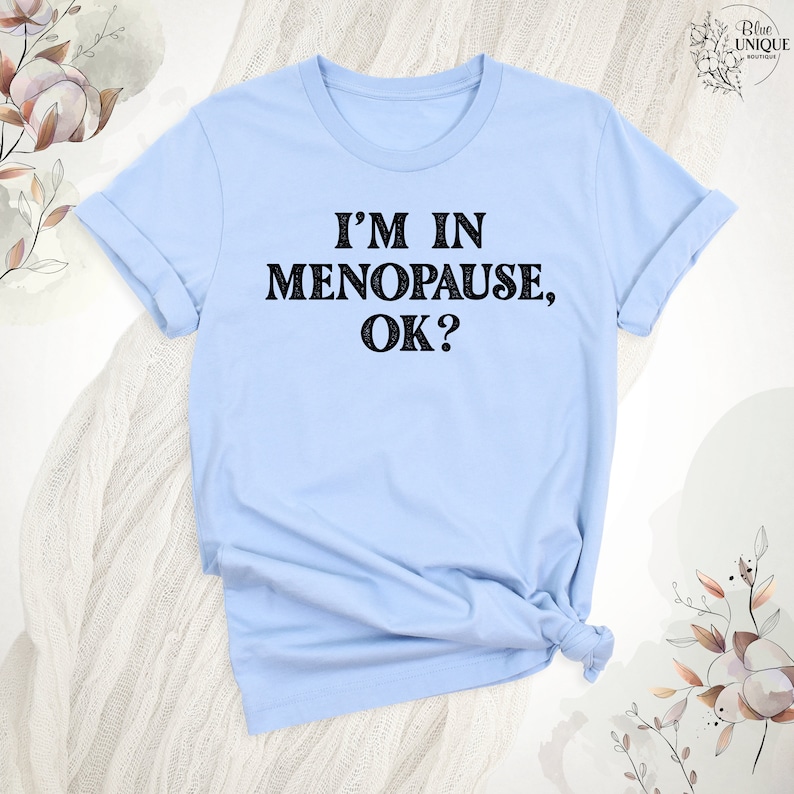 May include: A light blue t-shirt with the text "I'm in Menopause, OK?" printed in black.