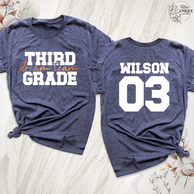 以下が含まれることがあります： ネイビーブルーのTシャツ2枚。1枚は白とオレンジの文字で「THIRD dream team GRADE」と書かれています。もう1枚は白で「WILSON 03」と表示されています。どちらのシャツも裾で結ばれています。学校やスポーツ活動に最適です。