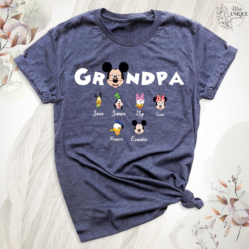 Puede incluir: Una camiseta azul marino con la palabra "Grandpa" en letras blancas. La camiseta presenta una imagen de dibujos animados de Mickey Mouse con otros seis personajes de dibujos animados debajo. Los nombres John, James, Lip, Luna, Robert y Edward est&aacute;n impresos debajo de los personajes.