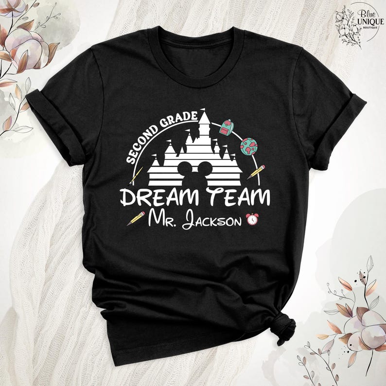 May include: Black t-shirt with a white graphic featuring a castle, Mickey Mouse ears, and the words "Second Grade Dream Team Mr. Jackson." The design includes pencils, a backpack, a globe, and an alarm clock.