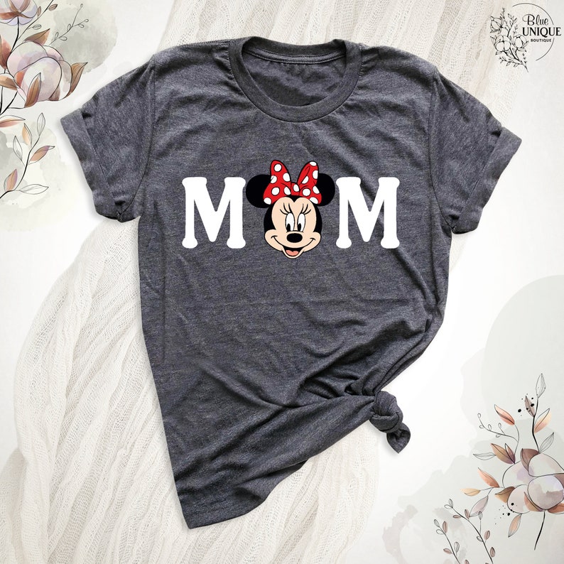 May include: Dark grey t-shirt with the word "MOM" and Minnie Mouse in the centre. Minnie Mouse has a red bow with white polka dots. The shirt is knotted at the bottom.