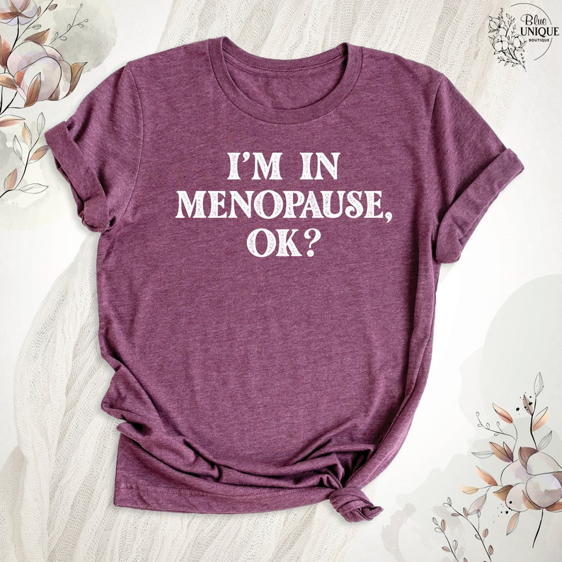 May include: A maroon t-shirt with the text "I'm in Menopause, OK?" printed in white.