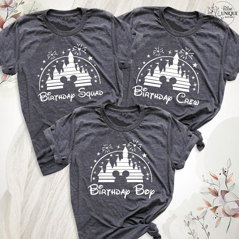 Pode incluir: Tr&ecirc;s t-shirts cinzas com uma silhueta branca do castelo da Cinderela e fogos de artif&iacute;cio. As t-shirts t&ecirc;m o texto "Birthday Squad", "Birthday Crew" e "Birthday Boy".
