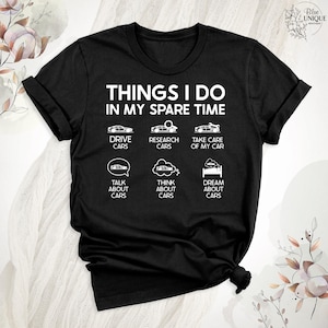 Op de afbeelding: Zwart T-shirt met witte tekst die "Things I do in my spare time" luidt. De tekst wordt omringd door zes witte pictogrammen die auto's voorstellen, waaronder rijden, onderzoek doen, zorgen voor, praten over, nadenken over en dromen over auto's.