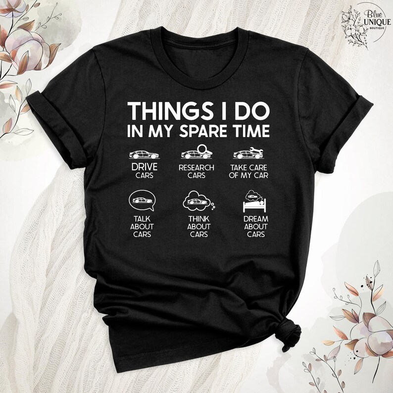Op de afbeelding: Zwart T-shirt met witte tekst die "Things I do in my spare time" luidt. De tekst wordt omringd door zes witte pictogrammen die auto's voorstellen, waaronder rijden, onderzoek doen, zorgen voor, praten over, nadenken over en dromen over auto's.