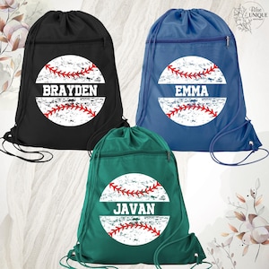 May include: Three drawstring backpacks in black, blue, and green, each featuring a circular graphic of a baseball with red stitching and a distressed white center. The names BRAYDEN, EMMA, and JAVAN are printed in white block letters across the center of each respective baseball design.