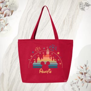 May include: Red canvas tote bag with a rainbow-colored castle graphic and the word "Auntie" in a whimsical font. The castle graphic is surrounded by stars and fireworks.
