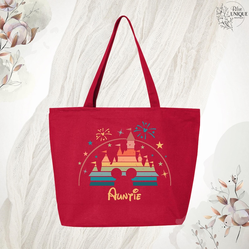 May include: Red canvas tote bag with a rainbow-colored castle graphic and the word "Auntie" in a whimsical font. The castle graphic is surrounded by stars and fireworks.