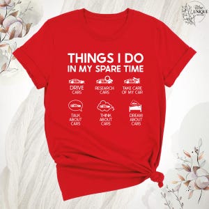 Op de afbeelding: Rood T-shirt met witte tekst die "Things I do in my spare time" zegt. De tekst is gerangschikt in een lijst met auto-iconen. De lijst bevat "Drive cars", "Research cars", "Take care of my car", "Talk about cars", "Think about cars" en "Dream about cars".