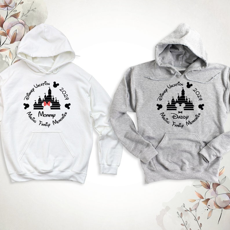 May include: Two hooded sweatshirts, one white and one gray, with a black and white graphic of Cinderella's castle, Mickey Mouse ears, and the text "Disney Vacation 2024 Making Family Memories". One sweatshirt says "Mommy" and the other says "Daddy".