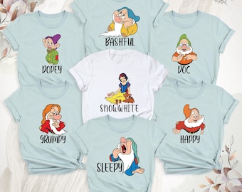 Könnte beinhalten: Eine Kollektion von sieben T-Shirts mit Schneewittchen und den sieben Zwergen. Sechs hellblaue T-Shirts zeigen einzelne Figuren mit den Aufschriften Dopey, Bashful, Doc, Grumpy, Happy und Sleepy. Ein weißes T-Shirt zeigt Schneewittchen.
