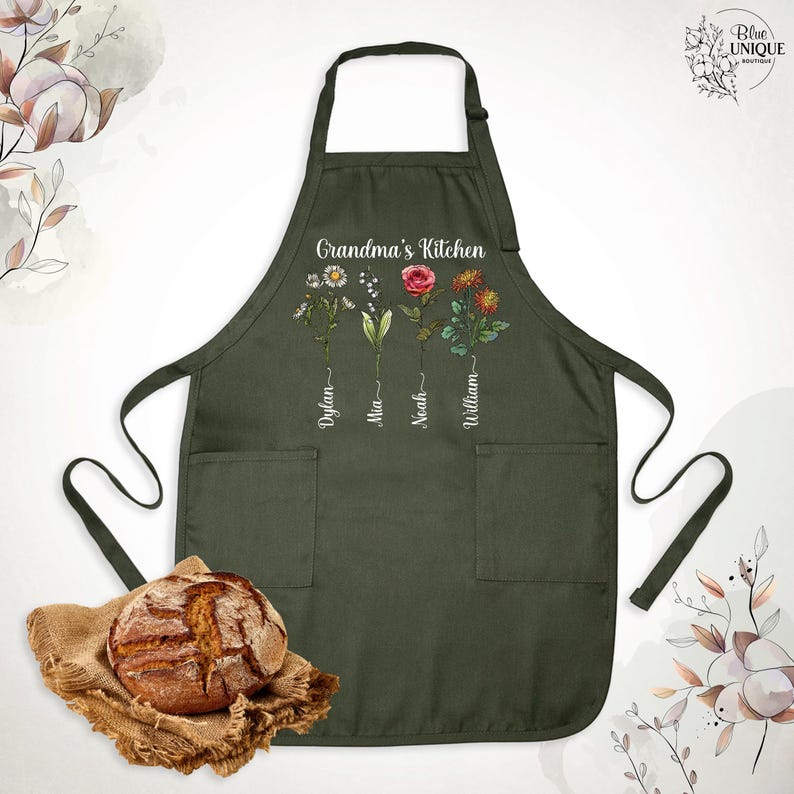 May include: Dark green apron with the text "Grandma's Kitchen" and floral designs. The apron has two pockets and features names: Dylan, Mia, Noah, and William. A loaf of bread rests on a burlap cloth.