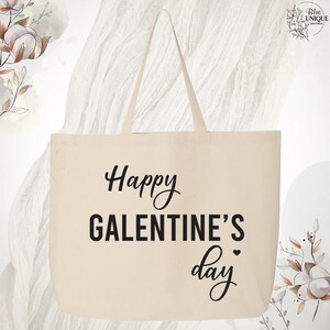 May include: Cream-colored tote bag with the text "Happy GALENTINE'S day" in black script and block letters. The bag has two handles and is made of a sturdy fabric. The design is simple and elegant.