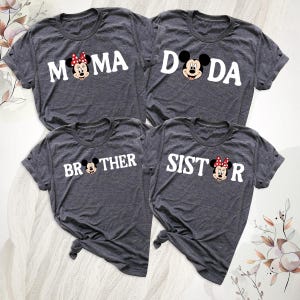 May include: Four grey t-shirts with white text and cartoon character graphics. The shirts read "MAMA," "DADA," "BROTHER," and "SISTER." The "MAMA" and "SISTER" shirts feature a character with a red bow. The t-shirts are knotted at the bottom.