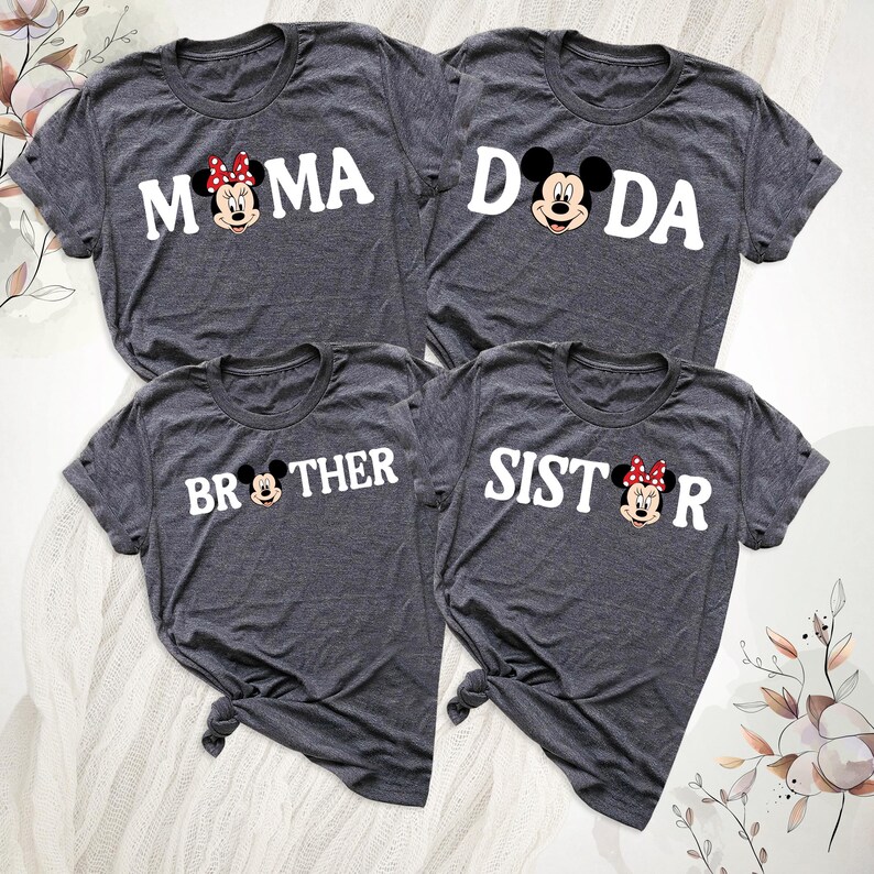 May include: Four grey t-shirts with white text and cartoon character graphics. The shirts read "MAMA," "DADA," "BROTHER," and "SISTER." The "MAMA" and "SISTER" shirts feature a character with a red bow. The t-shirts are knotted at the bottom.