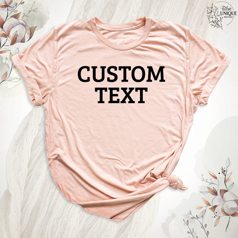 Może przedstawiać: Jasnor&oacute;żowy t-shirt z nadrukiem "CUSTOM TEXT" w kolorze czarnym.
