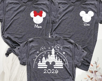 May include: Three dark heather gray t-shirts. Two shirts feature a white mouse head silhouette on the chest, one with a red bow and the text "Mom," the other with the text "Dad." The third shirt displays a white castle graphic with "2026."