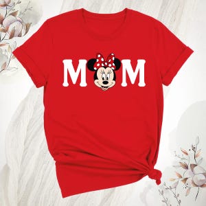 May include: A red t-shirt with the word "MOM" in white block letters, and Minnie Mouse's face in the centre. Minnie Mouse is wearing a red bow with white polka dots. The shirt is knotted at the bottom.