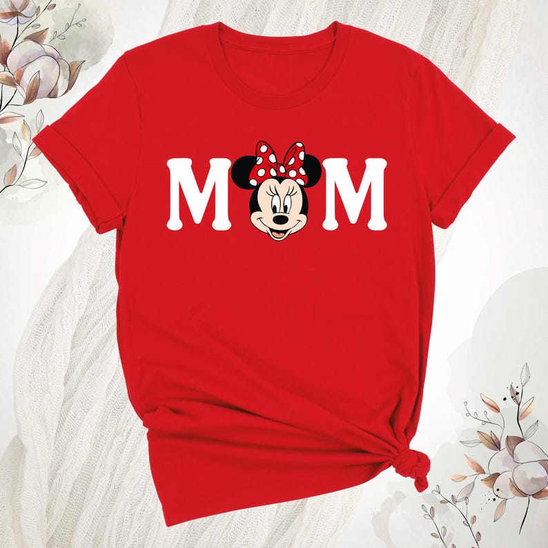 May include: A red t-shirt with the word "MOM" in white block letters, and Minnie Mouse's face in the centre. Minnie Mouse is wearing a red bow with white polka dots. The shirt is knotted at the bottom.