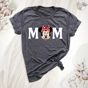 K&ouml;nnte beinhalten: Ein dunkelgraues T-Shirt mit einem wei&szlig;en Aufdruck von Mickey Mauses Kopf mit einer roten Schleife und wei&szlig;en Punkten. Der Aufdruck enth&auml;lt auch das Wort "MOM" in wei&szlig;en Buchstaben.