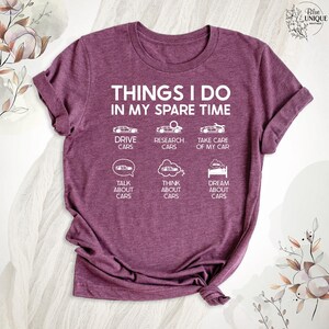 Op de afbeelding: Een maron T-shirt met de tekst "THINGS I DO IN MY SPARE TIME" en een lijst met autogerelateerde activiteiten, waaronder "DRIVE CARS", "RESEARCH CARS", "TAKE CARE OF MY CAR", "TALK ABOUT CARS", "THINK ABOUT CARS" en "DREAM ABOUT CARS".