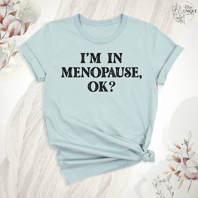 May include: A light blue t-shirt with the text "I'm in Menopause, OK?" printed in black.