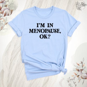 May include: A light blue t-shirt with the text "I'm in Menopause, OK?" printed in black.