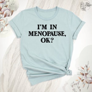 May include: A light blue t-shirt with the text "I'm in Menopause, OK?" printed in black.