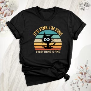 May include: Black t-shirt with a vintage-style graphic of a cat with big eyes and the text "It's fine, I'm fine, everything is fine".