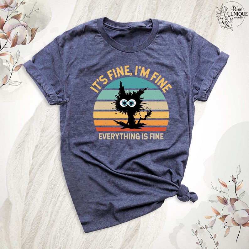 May include: A navy blue t-shirt with a vintage-style graphic of a black cat with big eyes and the text "It's fine, I'm fine, everything is fine".