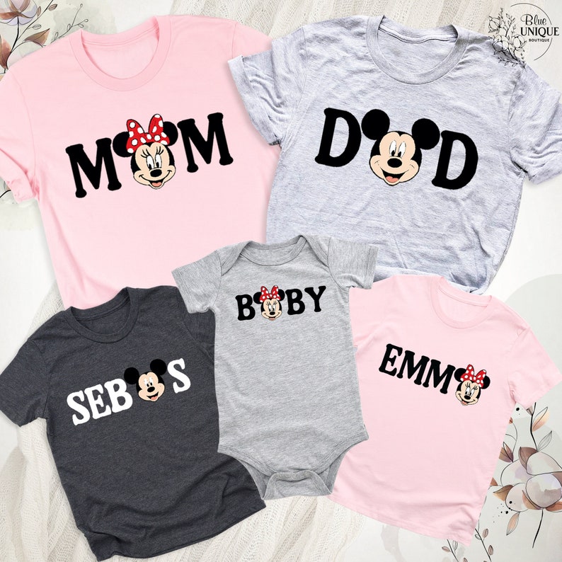 May include: A selection of family matching t-shirts and a baby onesie. The shirts are pink, grey, and dark grey, with the words "MOM", "DAD", "SEB", and "EMM" printed. The baby onesie is grey and says "BABY". Each item features a Minnie Mouse graphic.