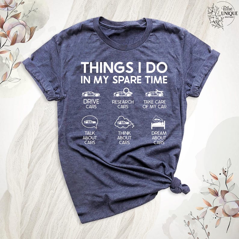 Op de afbeelding: Een marineblauw T-shirt met witte tekst die "Things I do in my spare time" luidt. De tekst wordt omringd door zes pictogrammen die auto's voorstellen, waaronder rijden, onderzoek doen, zorgen voor, praten over, nadenken over en dromen over auto's.