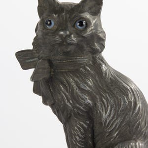 May include: A detailed, antique-style cat figurine with a dark, metallic finish. The cat has bright blue eyes and a bow around its neck. The figurine is a decorative item, likely for display.