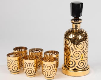 May include: A set of six gold-rimmed glasses with a swirling pattern and a matching gold decanter with a black stopper.