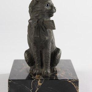 May include: A dark grey cat ornament with a bow tie, sitting on a black marble base. The cat has blue eyes and is looking to the side. The marble base has gold veining.