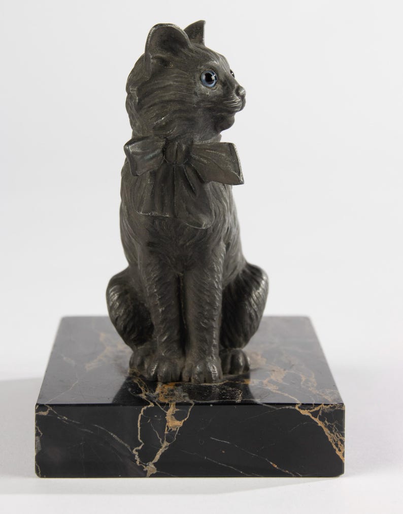 May include: A dark grey cat ornament with a bow tie, sitting on a black marble base. The cat has blue eyes and is looking to the side. The marble base has gold veining.