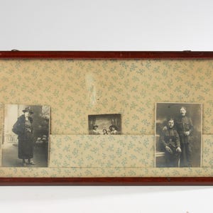 May include: A rectangular wooden frame with a floral patterned background holds three black and white photographs. The frame has a dark brown finish and decorative metal accents. The photographs depict people in vintage clothing.