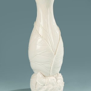 May include: A tall, white ceramic vase with a leaf-like design. The vase has a ruffled rim and a bulbous base with a textured, organic appearance. The leaves are intricately detailed, adding to the vase's elegant aesthetic.
