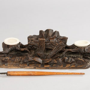 Pode incluir: Um tinteiro de madeira castanho escuro com dois tinteiros de porcelana branca e um porta-canetas de madeira. O tinteiro é esculpido com detalhes intrincados e tem um aspecto rústico.