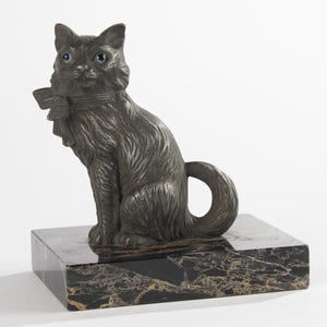 May include: A dark grey cat ornament with blue eyes and a bow, sitting on a black and gold marble base. The cat has detailed fur and a curled tail. This decorative sculpture is a unique home decor item.